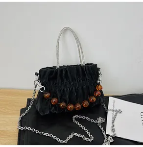 Detail of black pleated handbag featuring silver bead handle and orange decorative beads