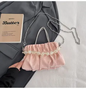 Detail of light pink ruched handbag with bead handle and silver chain on textured fabric