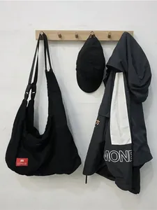 Large black canvas hobo bag with adjustable wide strap and red woven label on white wall