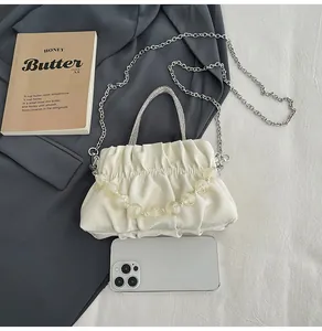 Detail of white pleated handbag with rhinestone handle and yellow bead chain strap
