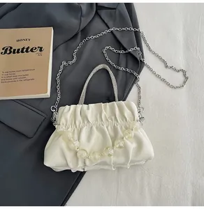 Detail of white pleated handbag with rhinestone handle and large bead decoration