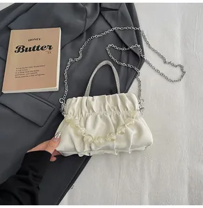 Close-up of pleated beige cloud bag with rhinestone handles and beaded chain detail