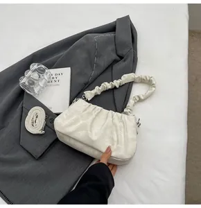 Detail of beige ruched cloud bag on white fabric background with stylish props