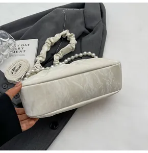 Detail of cream pleated cloud bag with pearl handle and marble texture on blazer background