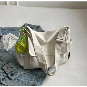 Detail van witte canvas schoudertas met groene pluche bloemenhanger en brede schouderriem