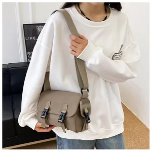 Close-up of a khaki nylon messenger bag with black buckles on a model in a casual setting