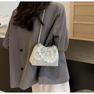 Silberne Falten-Cloud-Tasche mit Perlen Griff und Metallkette auf grauem Blazer