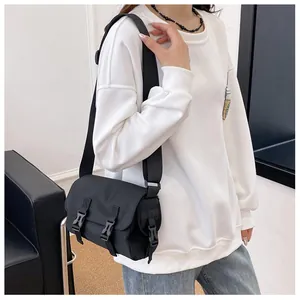 Detail view of a black canvas messenger bag with dual buckle closure on a casual outfit