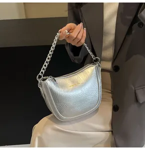 Detail of silver metallic textured handbag with chunky chain handle and brand logo