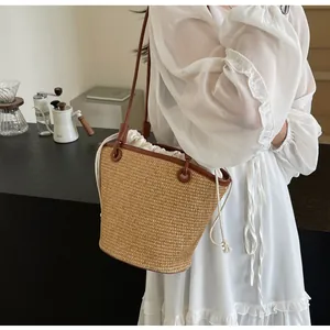 Detail of woven straw bucket bag with brown leather trim held by a woman in white dress