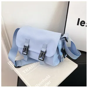 Detailed view of light blue canvas messenger bag with black buckles on white background