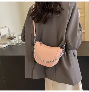 Pink crescent crossbody bag with chunky silver chain shown on model in a cafe setting