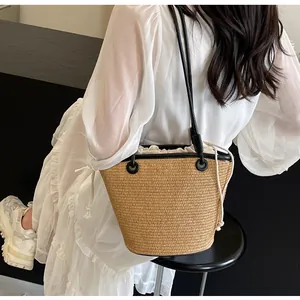 Detail of woven straw bucket bag with black leather strap and white drawstring liner