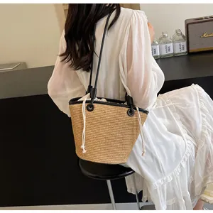 Detail of a woven straw bucket bag with black trim and drawstring liner on a model