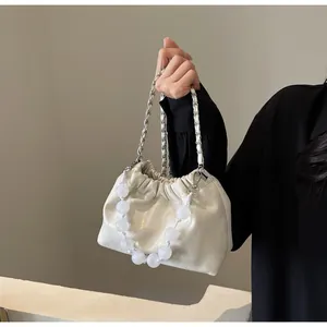 Detail einer cremeweißen Falten-Beuteltasche mit großen Perlen und Kettenschultergurt