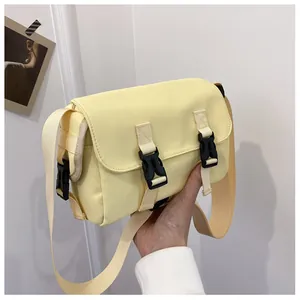 Detail of light yellow canvas messenger bag featuring black plastic buckles and adjustable strap