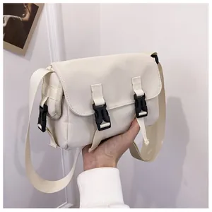 Close-up of cream messenger bag with double black buckles and adjustable strap
