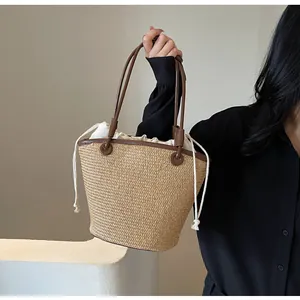 Detail of woven straw tote bag featuring brown leather straps and inner drawstring pouch