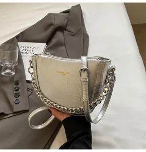 Close-up of silver crescent bag with metallic pleats and chunky chain on grey blazer