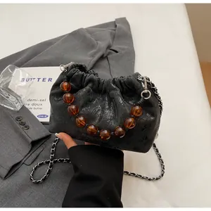 Detail der schwarzen Bucket Bag aus Lackleder mit Bernstein-Perlengriff und Metallkette