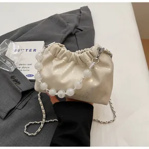 Detailansicht der cremefarbenen Beuteltasche mit Perlengriff und Silberkette