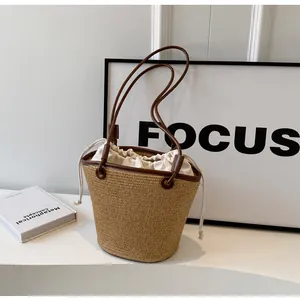Detail of woven straw bucket bag showing brown leather trim and canvas drawstring liner