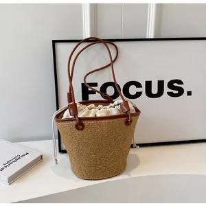 Detail of hand-woven straw bucket bag with dark brown leather trim and white canvas drawstring liner