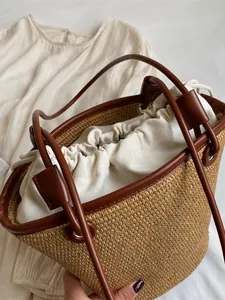 Handwoven straw bucket bag with dark brown leather handles and a canvas drawstring liner