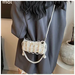 Détail d'un sac à bandoulière en perles blanches fait main porté sur un blazer gris