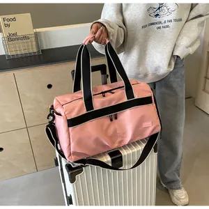 Rosa wasserdichte Reisetasche mit schwarzen Tragegriffen und Gurt neben einem Koffer