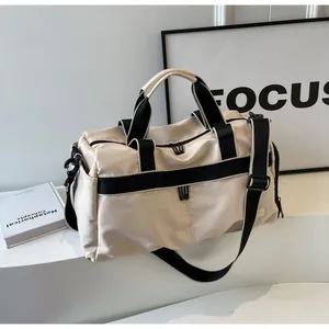 Detailansicht der beigen Reisetasche mit schwarzen Gurtbändern und abnehmbarem Schultergurt