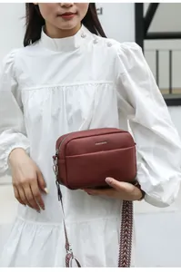Détail du sac bandoulière bordeaux avec texture litchi et sangle tissée sur modèle