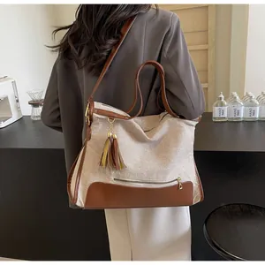 Detail of canvas bag featuring brown leather trim, decorative tassels, and adjustable strap