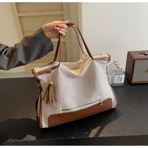 Detail of canvas tote bag with brown leather trim and tassel on a stylish beige fabric