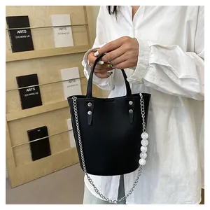Detail of black pebbled leather bucket bag featuring elegant bead and chain strap accents