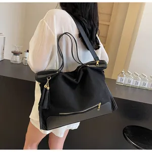 Detail of a large black canvas tote bag with tassel charm worn by a model in a room