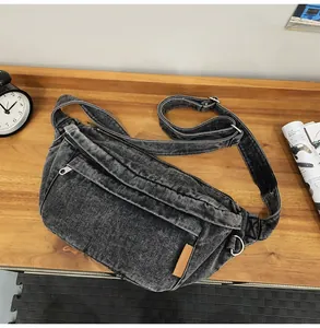 Detail van grijze denim crossbodytas met verstelbare riem en lederen label erop