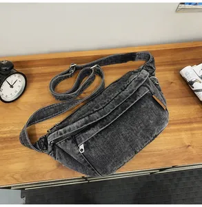 Detail van donkergrijze denim crossbody tas met verstelbare riem en metalen ritssluitingen