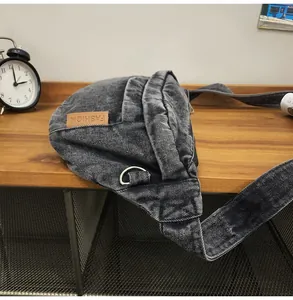 Detail van donkergrijze denim borsttas met leren patch op een houten tafeloppervlak