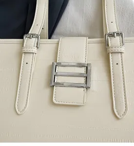 Detailed close-up of cream leather tote bag with silver metal buckles and textured finish