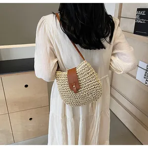 Détail d'un sac bandoulière en paille tressée avec garniture en cuir brun et bouton