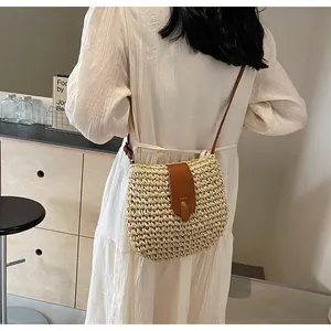 Détail d'un sac bandoulière beige en paille tressée porté par un mannequin en décor épuré