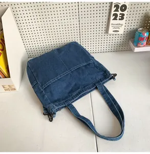 Dettaglio della borsa tote in denim blu scuro con cuciture a contrasto e fibbia laterale