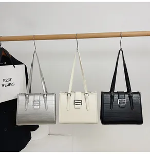 Three textured leather tote bags in silver, beige, and black colors hanging on a wooden rack