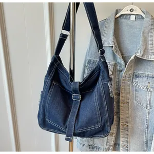Detail of dark blue denim hobo bag with distressed edges and adjustable straps