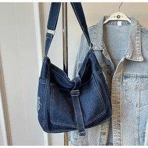 Detail of dark blue denim crossbody bag with white stitching and frayed edge texture