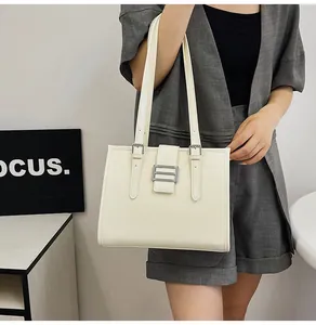 Detail of cream faux leather tote bag with metal buckle and shoulder straps on a model