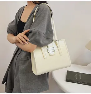 Detail of cream-colored crocodile texture tote bag with silver buckle on grey suit model