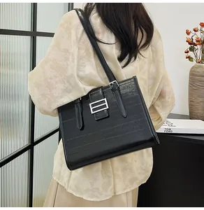 Detail of the black textured leather tote bag with silver buckle worn by a model