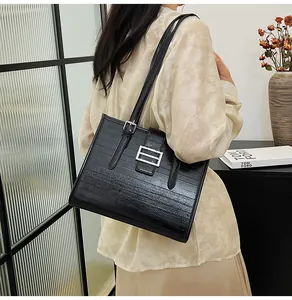Detail of black tote bag with silver buckle and glossy texture shown on shoulder